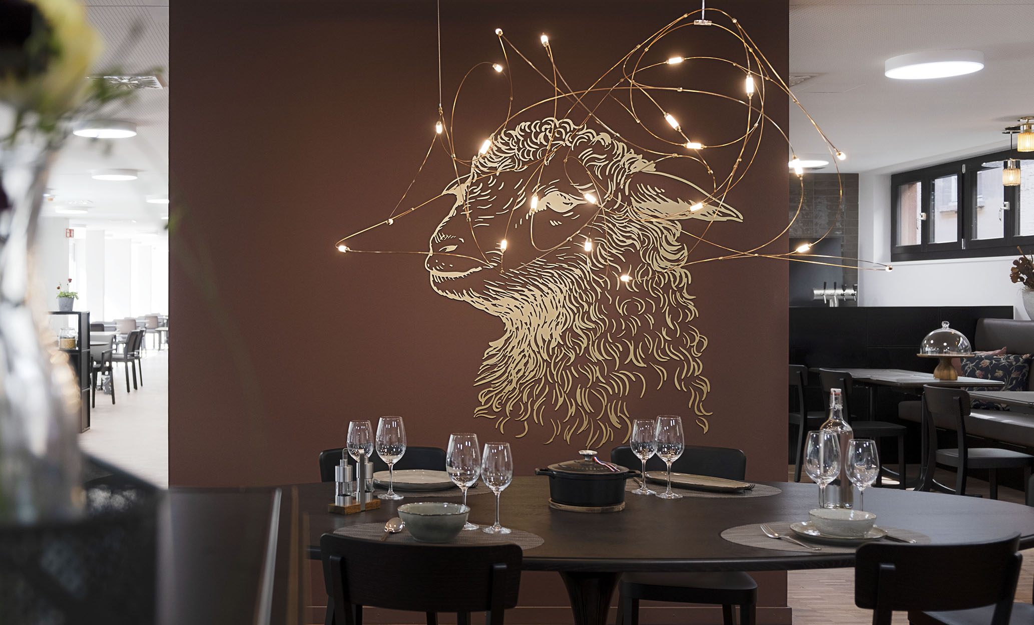 Ein gedeckter Tisch im Restaurant zum Lamm, dahinter an einer braunen Wand das Emblem, ein Lamm in heller Farbe