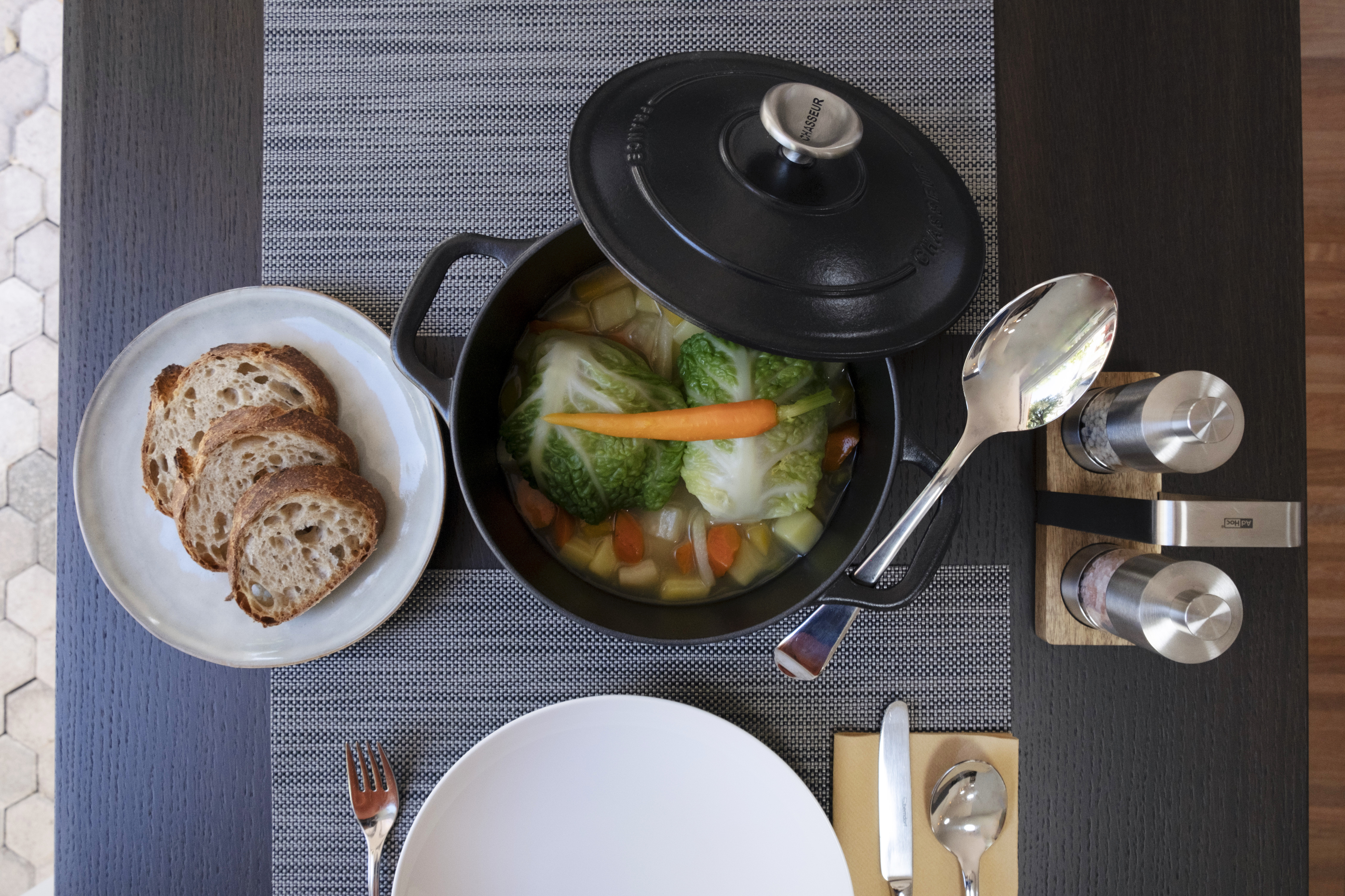 Ein gedeckter Tisch von oben, In der Mitte steht eine offene Pfanne mit Gemüsesuppe